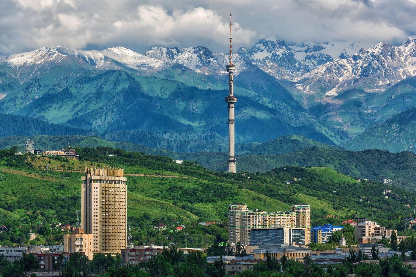 The Almaty TV tower with snowy mountains behind the city