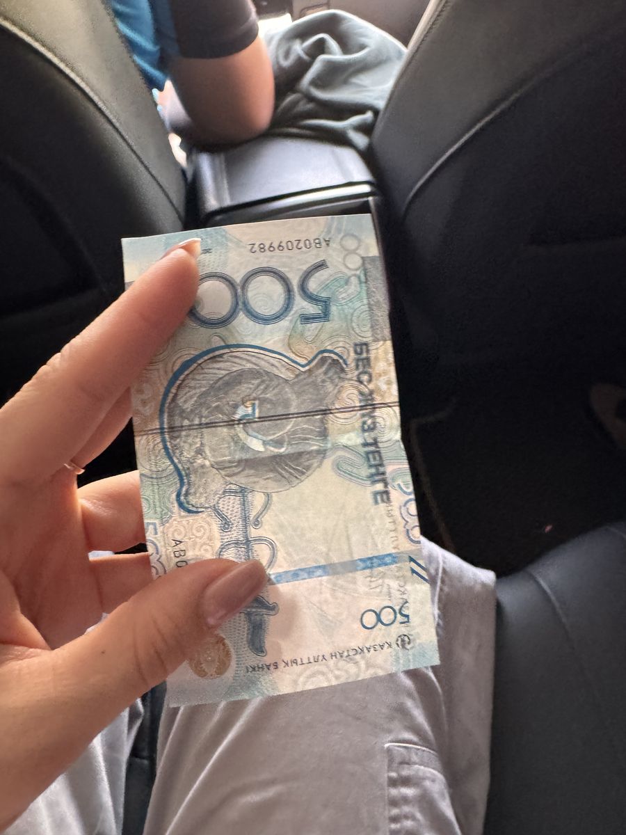 A hand holding a 500-tenge banknote